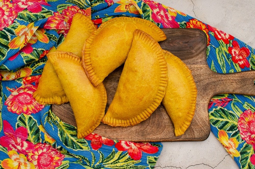 Image of Jamaican patties on a wooden board surrounded by a flower patterned cloth.